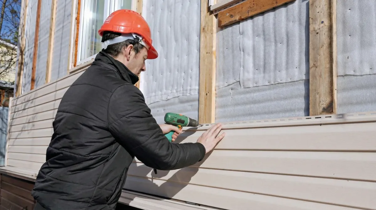 Siding replacement professional using a power drill to install new tan vinyl siding on a home exterior in Long Beach, CA